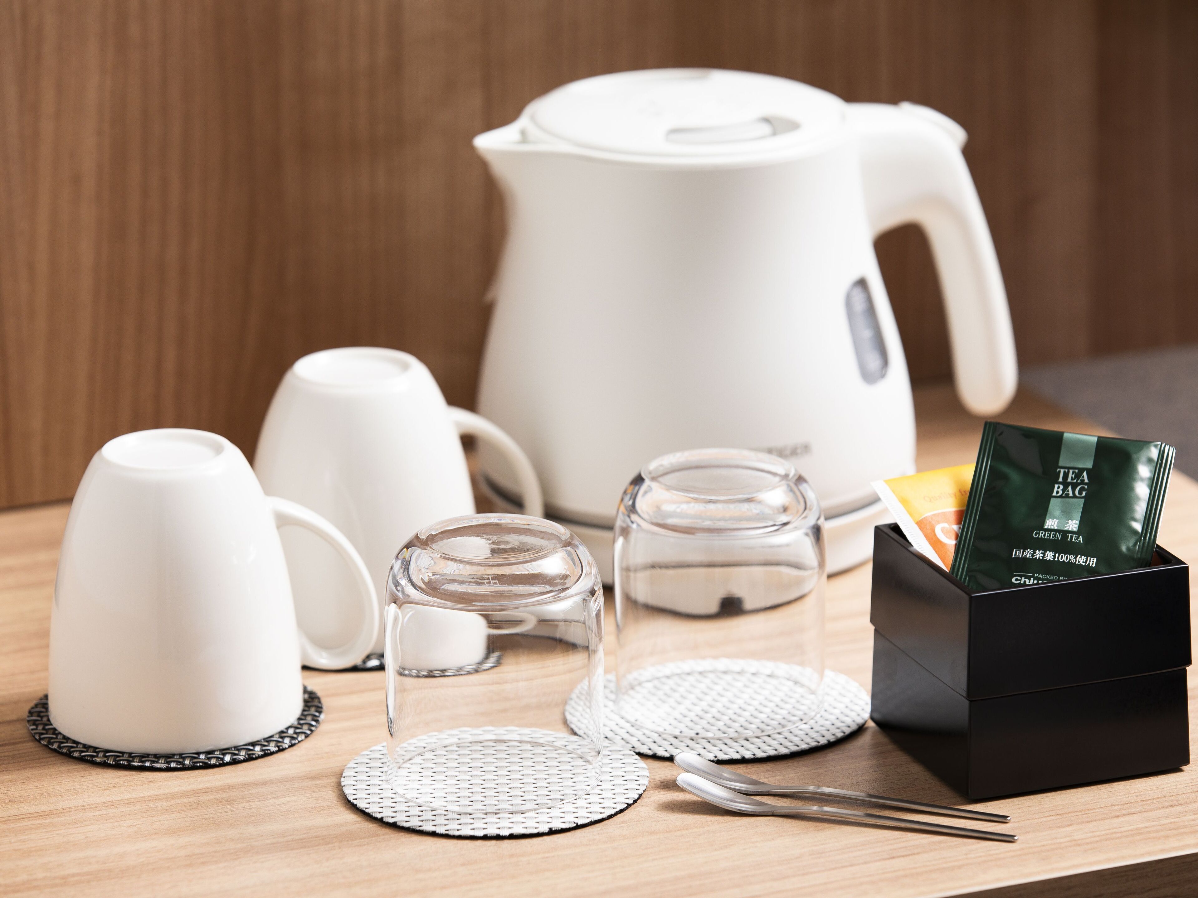 A tea set including a white teapot, cups, a glass, a tea bag box, and a tea infuser on a wooden table.