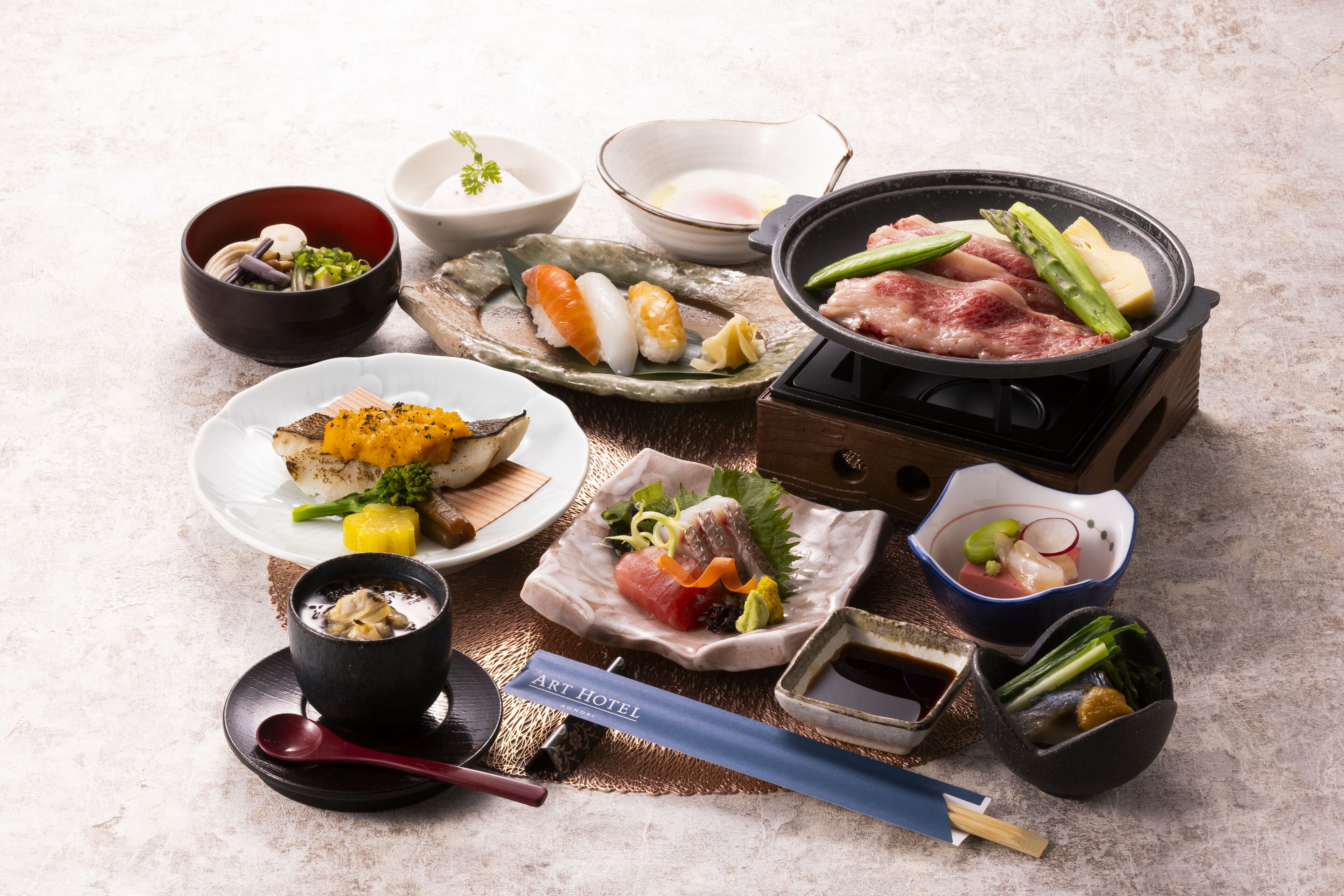 A variety of Japanese dishes, including sushi and sashimi, arranged on a table with a hot pot and condiments.