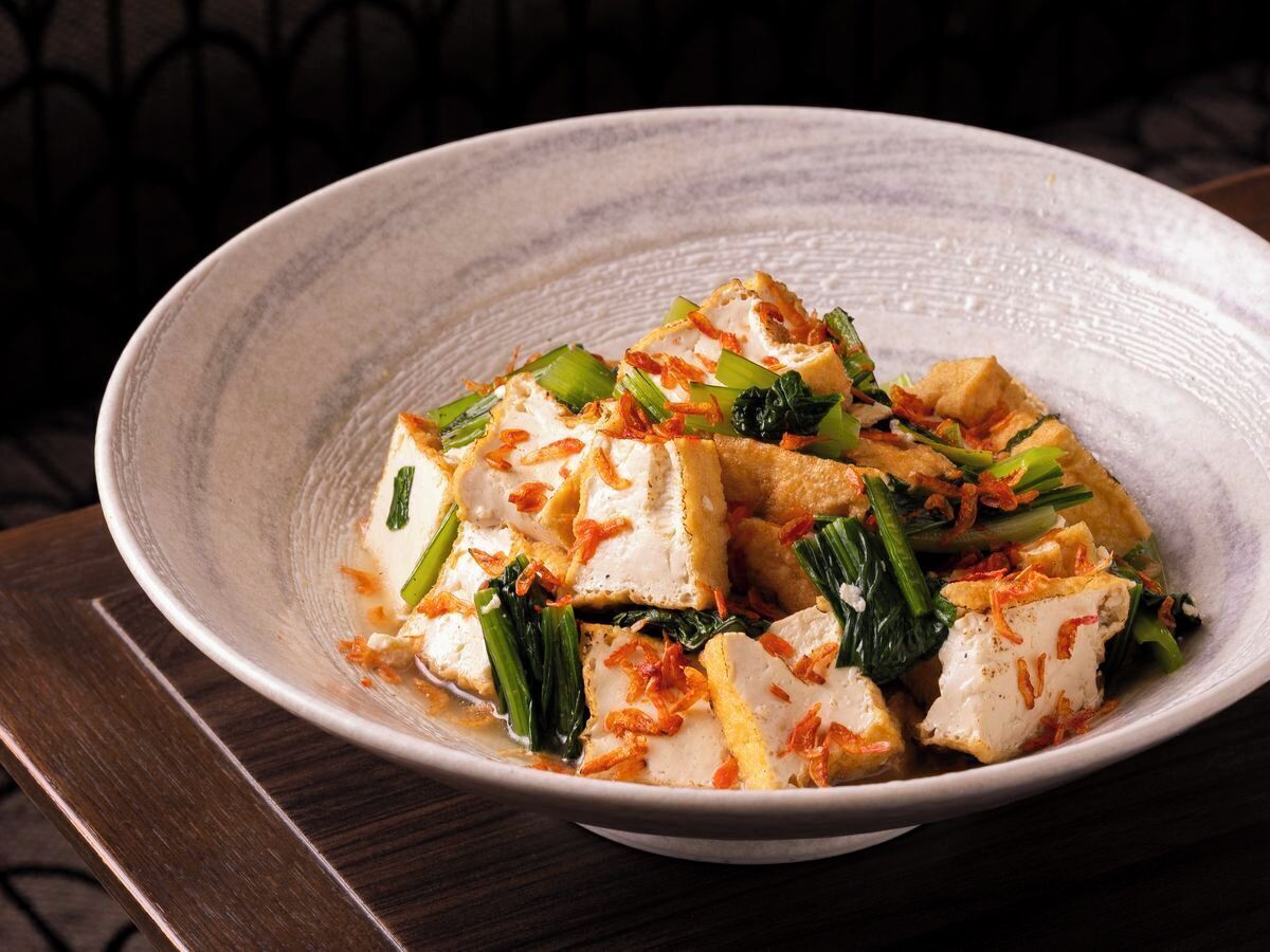 Un plato de tofu con verduras y cebollas fritas.