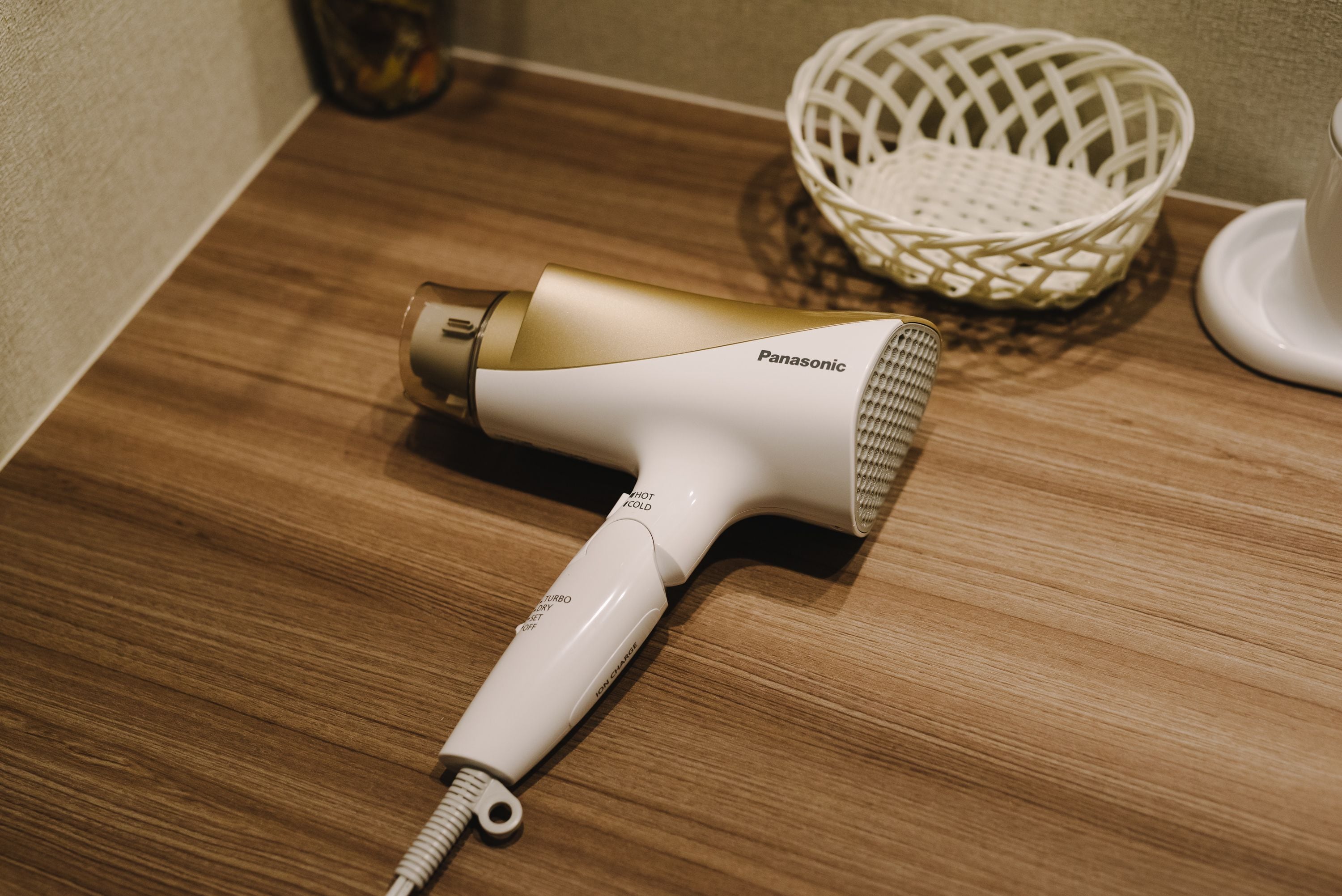 A Panasonic hair dryer on a wooden surface with a woven basket in the background.