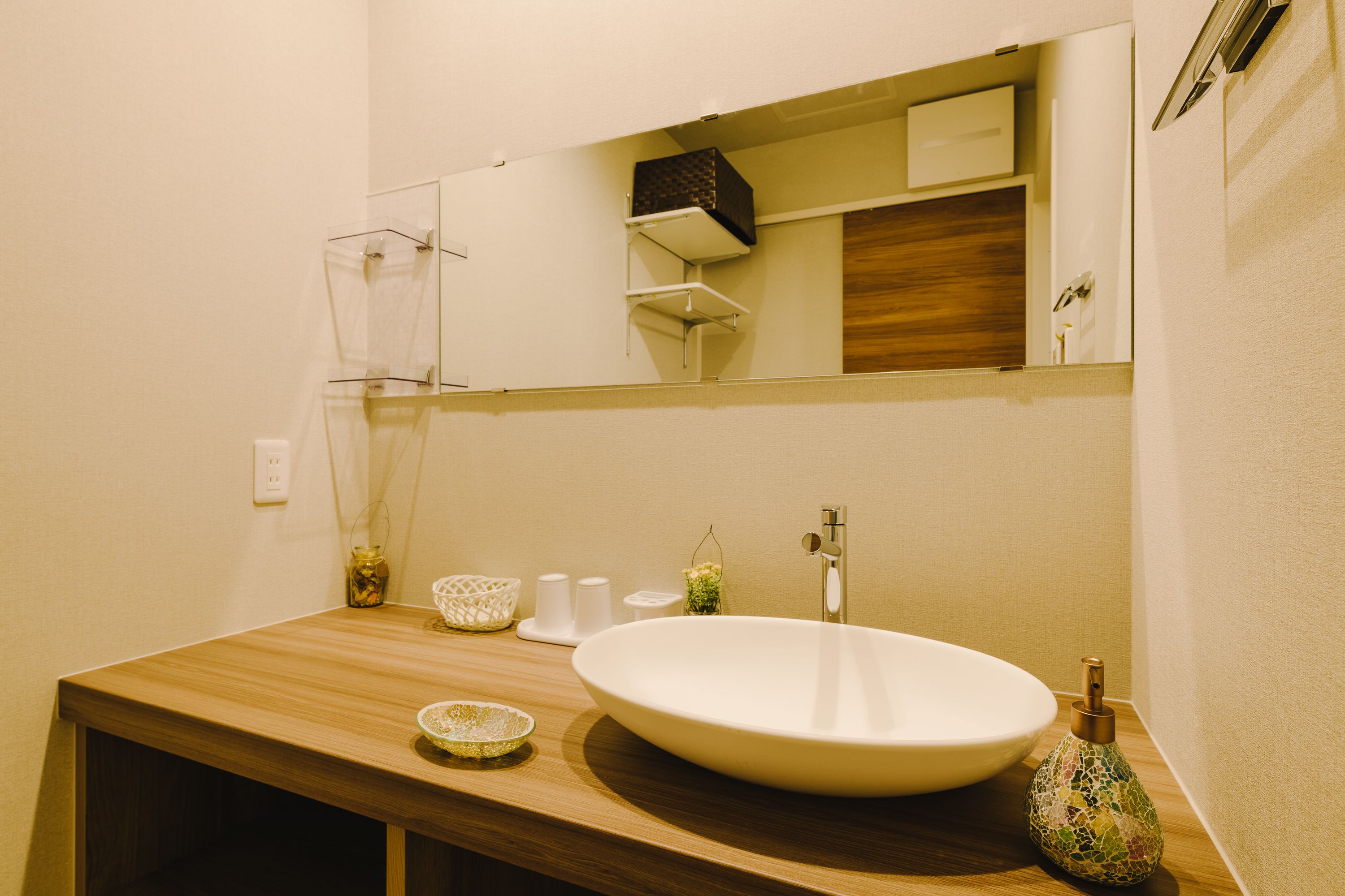 A bathroom with a wooden vanity, a large white sink, a mirror, and a small decorative vase.