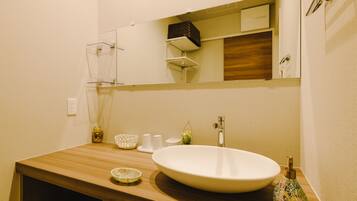 A bathroom with a wooden vanity, a large white sink, a mirror, and a small decorative vase.