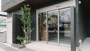 A modern building with a large glass door entrance, a small tree, and a metal fence.