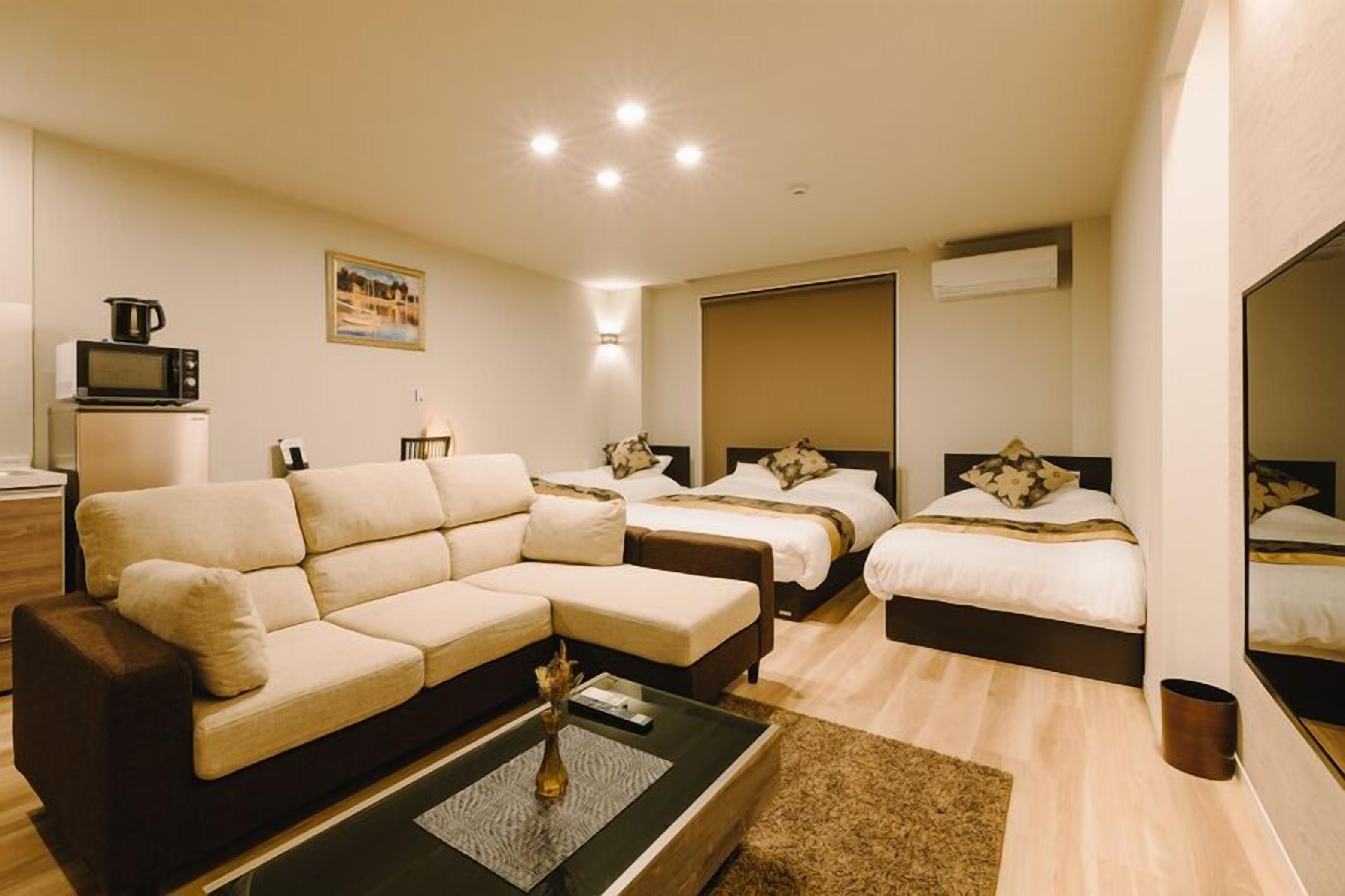 A modern hotel room with a sofa, two beds, a coffee table, and a painting on the wall.