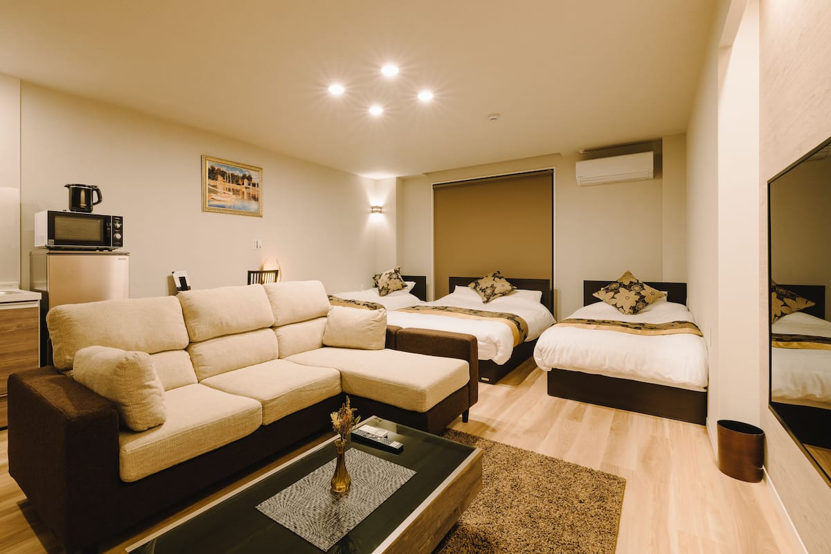 A modern hotel room with a sofa, two beds, a coffee table, and a painting on the wall.