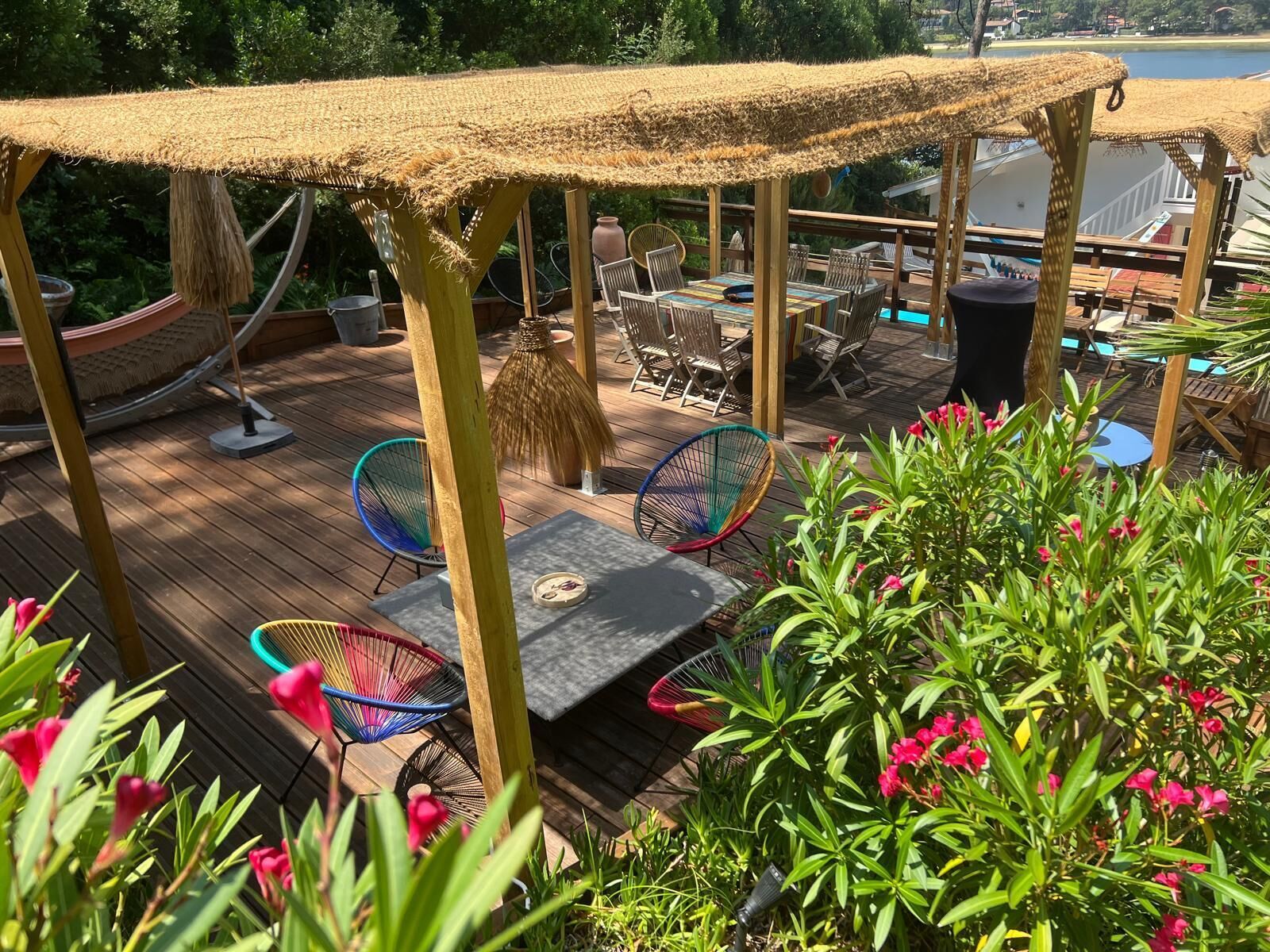 Um deck de madeira com móveis para área externa, um telhado de palha e vista para um corpo d'água.