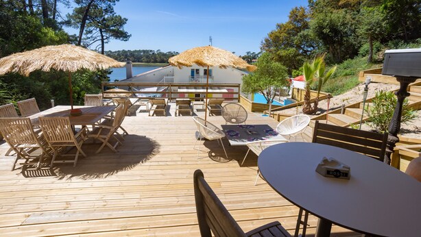 A wooden deck with outdoor furniture, including tables and chairs, and a thatched umbrella.