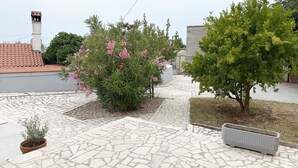 Une cour avec un sol carrelé, un pot de fleurs, un arbre aux fleurs roses et un bâtiment avec un toit en tuiles.
