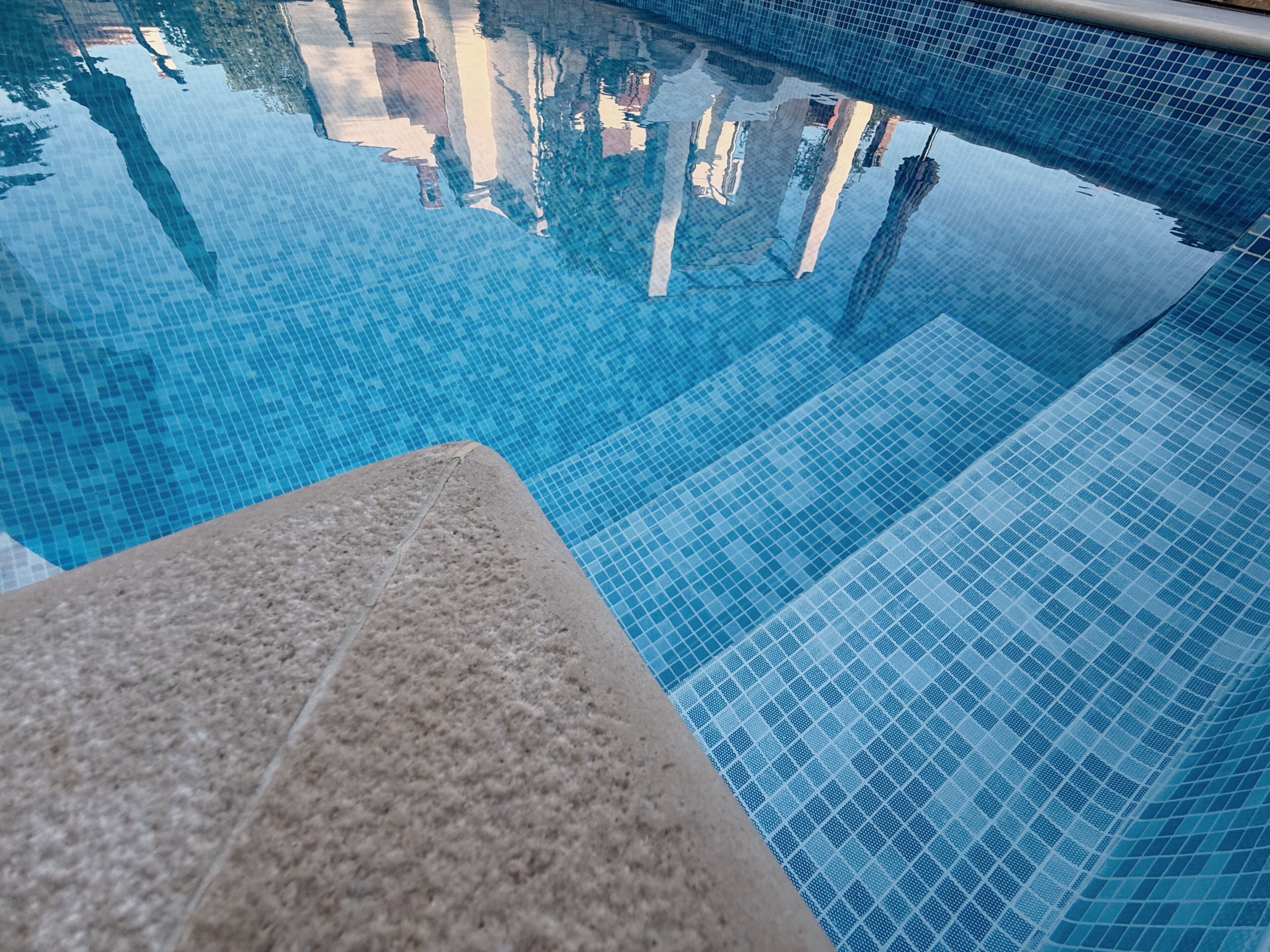 A clear view of a swimming pool with a tiled edge and a stone ledge.