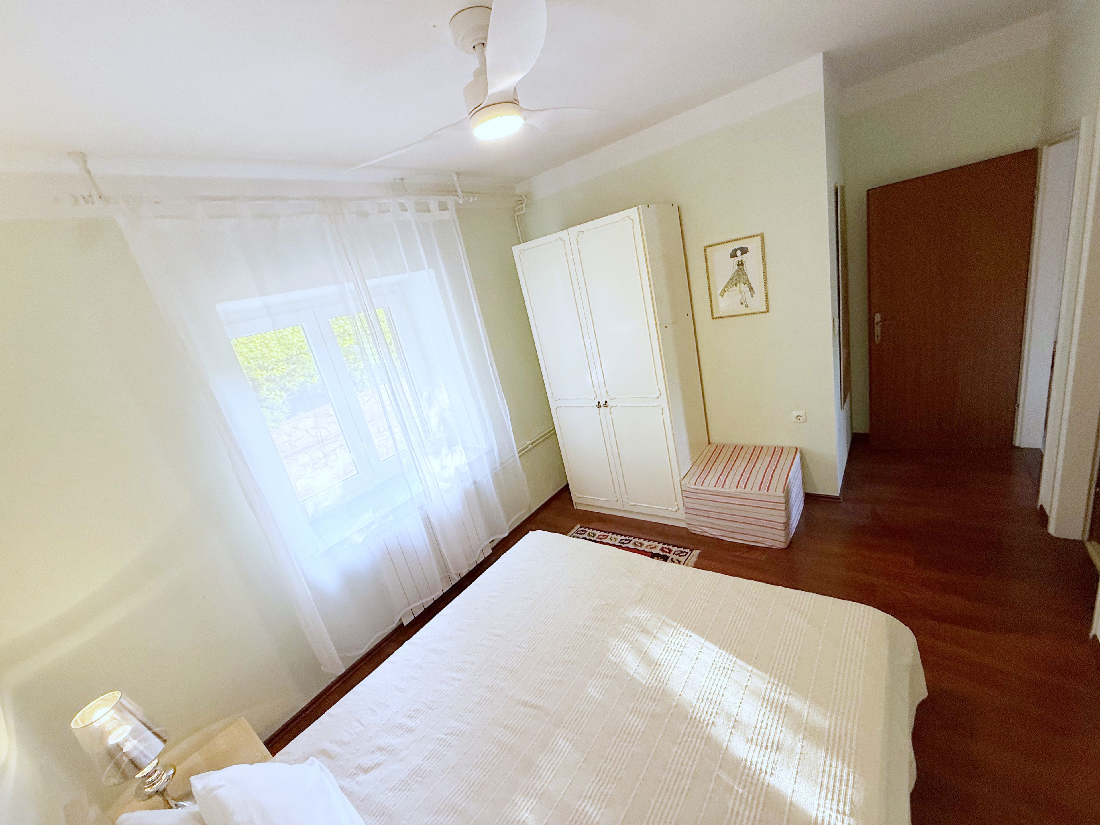 Un dormitorio con cama, armario, mesita de noche y ventana con cortinas.