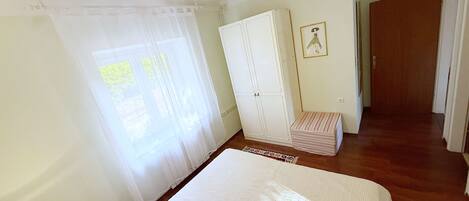 Un dormitorio con cama, armario, mesita de noche y ventana con cortinas.