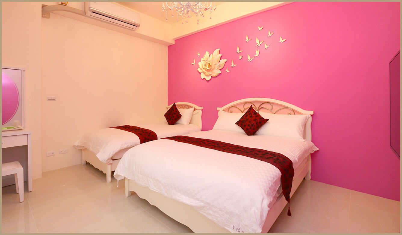 A double bed with white bedding and red accents, a small bedside table, and a wall with a floral decoration and butterfly art.