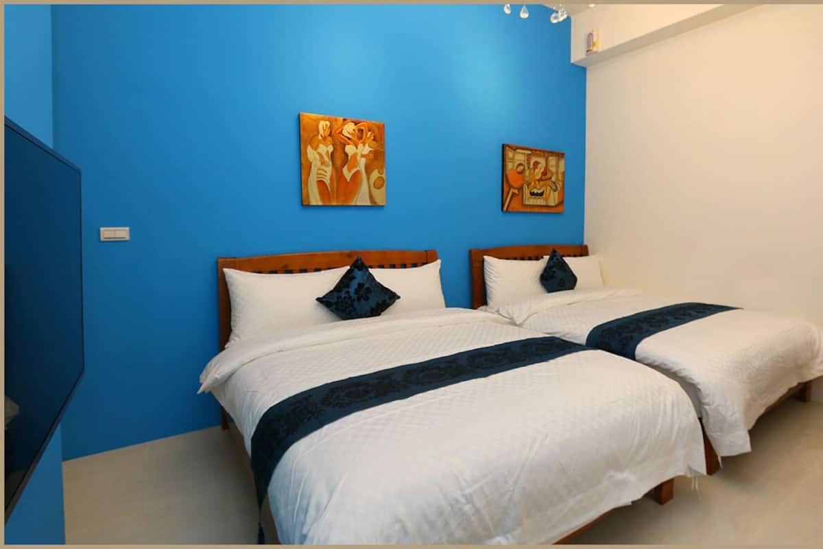 A room with two beds, blue walls, and artwork on the wall.