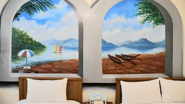 A room with two beds, each with a view through an arched window. One window shows a beach scene with a sailboat and umbrella, the other shows a lakeside scene with boats. - When Happiness Knock Your Door (Hualien City)