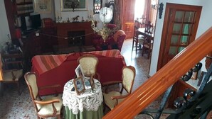Ein Zimmer mit einem roten Sofa, Holzstühlen, einem Tisch mit weißer Spitzenleinentuch und einer Kristallleuchter.