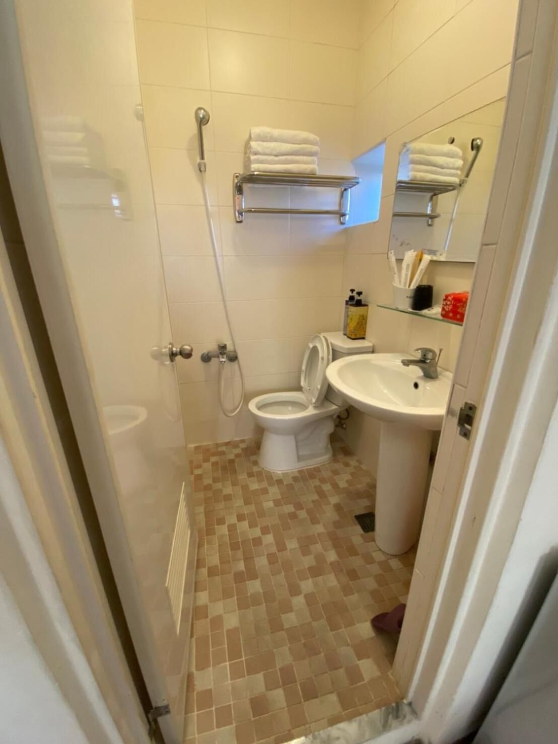 A small bathroom with a toilet, sink, and shower. There are towels on a shelf above the toilet.