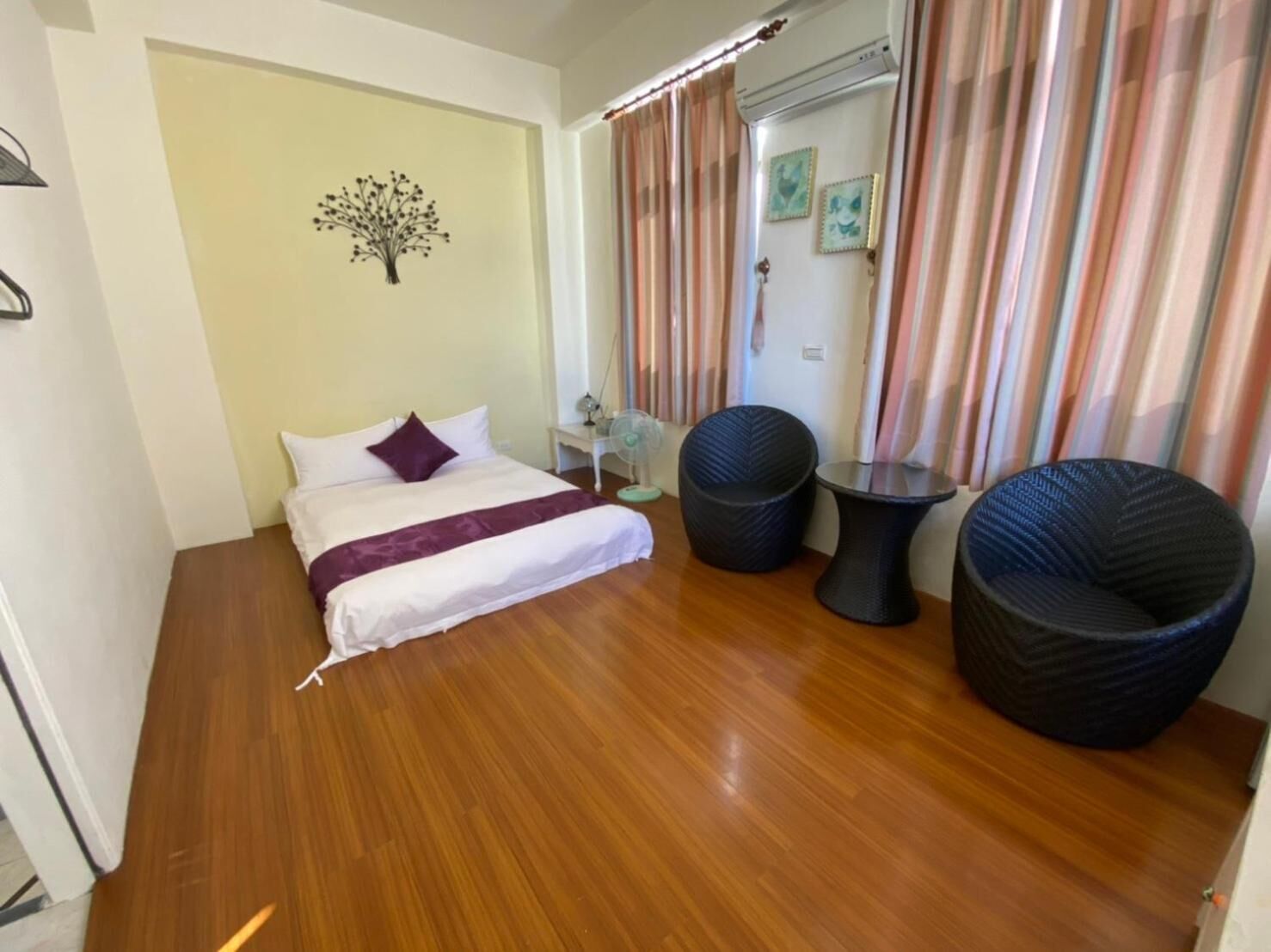 A bedroom with a bed, two chairs, a small table, and a wall-mounted air conditioner.