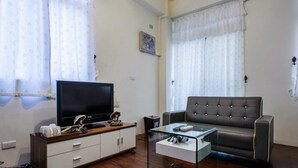 A living room with a flat-screen TV, a leather sofa, a glass coffee table, and a wooden cabinet. - 19 wuo wuo hotel (Hualien City)