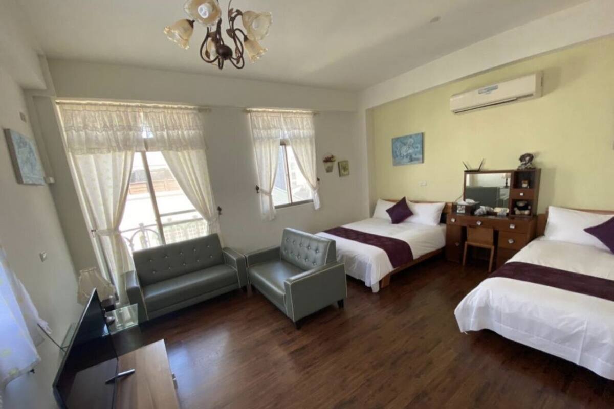 A hotel room with two beds, a desk, a chair, and a sofa.