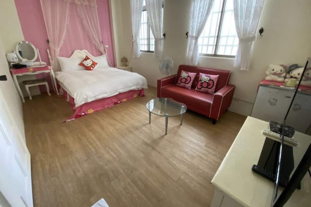 A bedroom with a bed, a red sofa, a glass coffee table, and a desk with a computer.