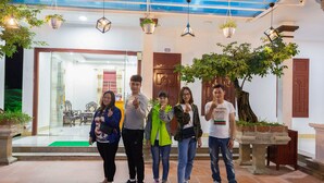 A group of people standing in a lobby with a glass door entrance, hanging lights, and potted plants.