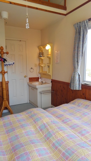 Un dormitorio con cama, armario de madera, espejo, lavabo y ventana con cortinas.