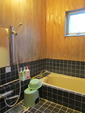 Un baño con pared de madera, una bañera, un taburete verde y un ventanal.