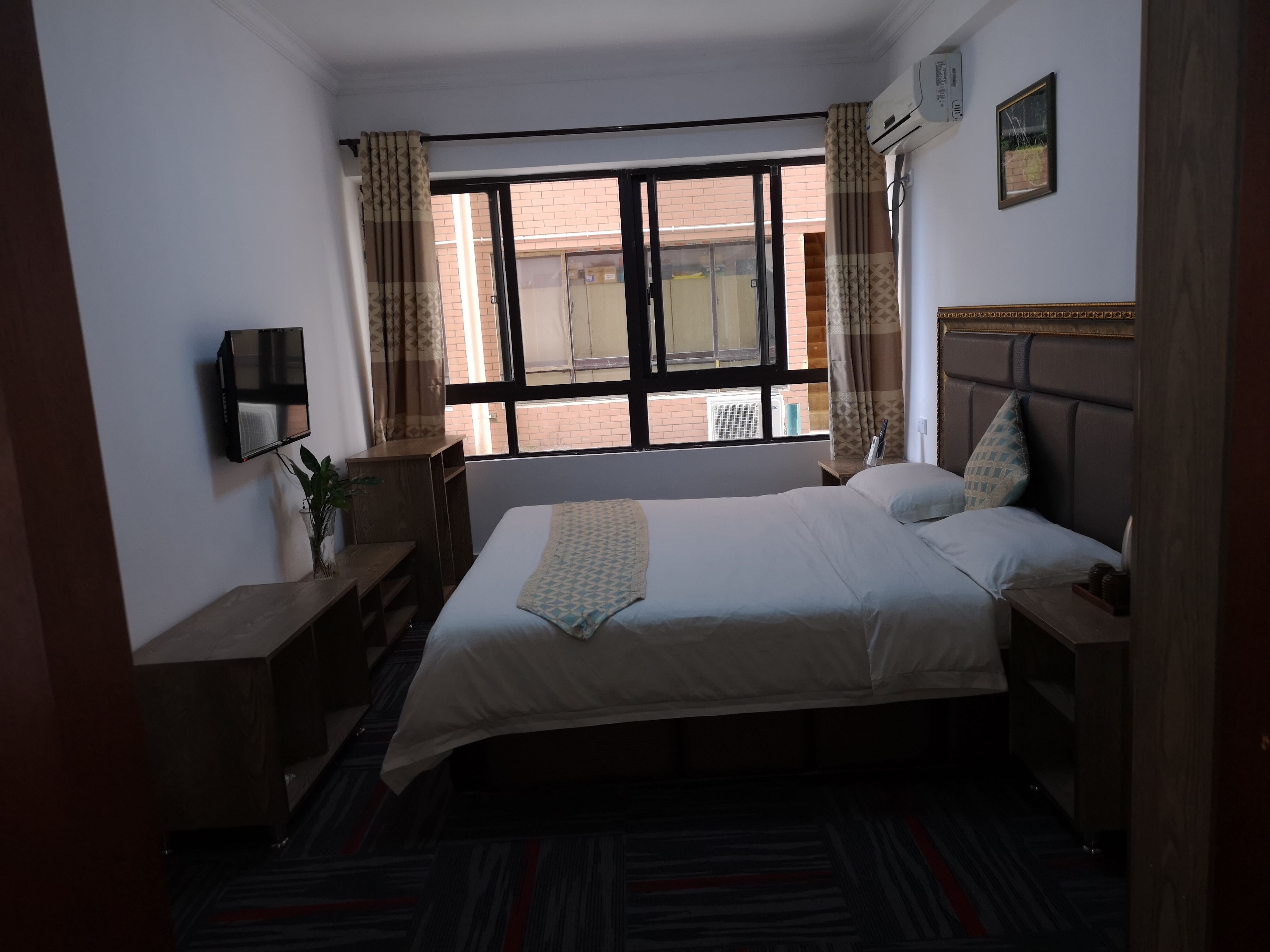A hotel room with a bed, a desk, a chair, a TV, and a window with curtains.