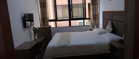 A hotel room with a bed, a desk, a chair, a TV, and a window with curtains.