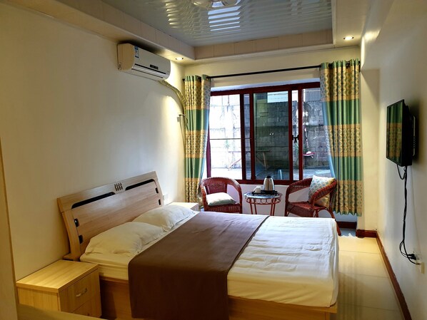 A bedroom with a bed, bedside tables, a small table with a kettle, chairs, and a TV.