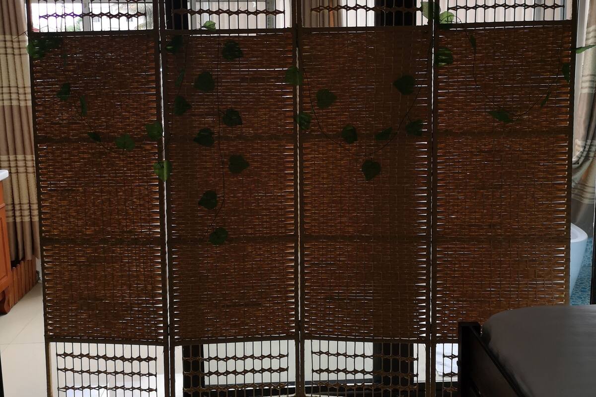 A room with a large bed, a sliding door with a woven pattern, and a view of the outside through the door.