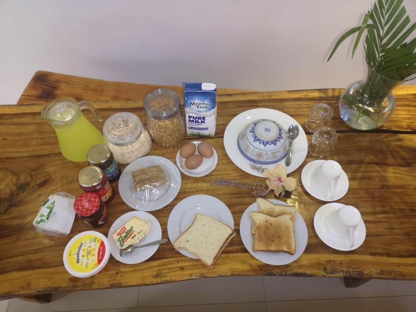 A wooden table with breakfast items including bread, eggs, butter, jam, and milk.