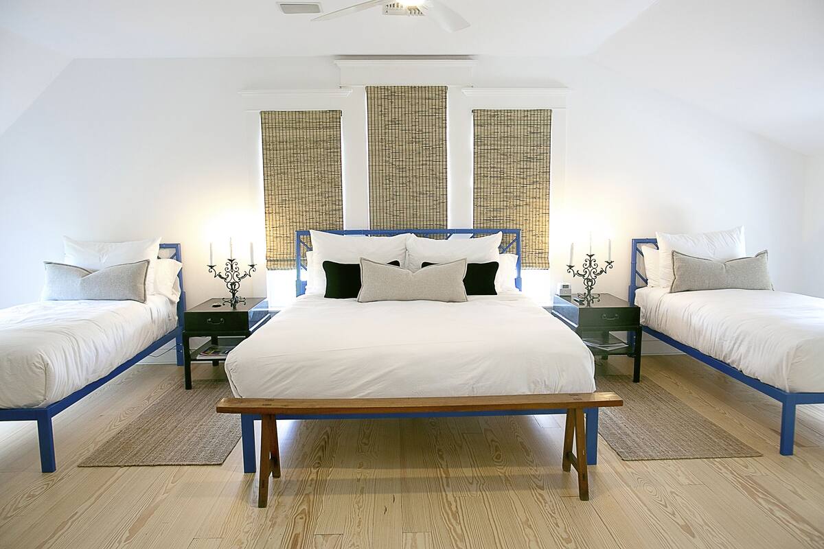 A bedroom with a central bed flanked by two smaller beds, a wooden bench, and a ceiling fan.