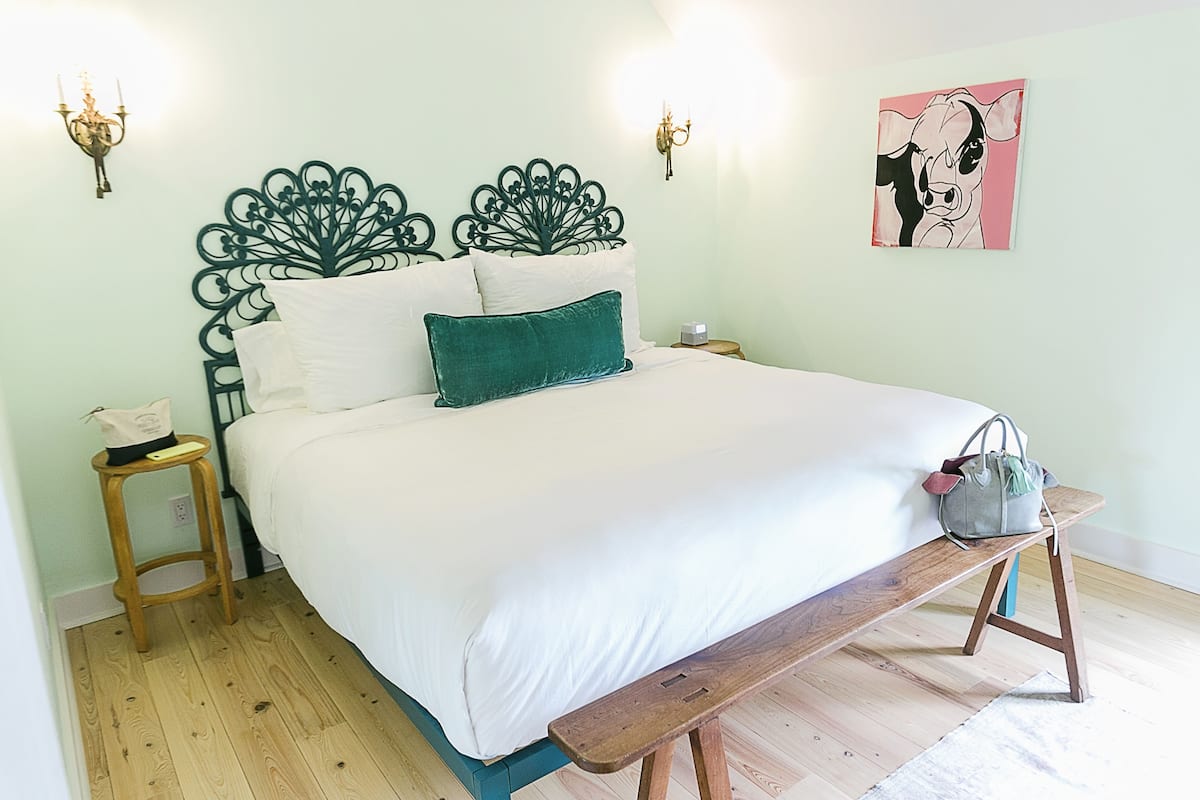 A neatly made bed with a wooden bench, a bedside table, and a wall-mounted lamp.