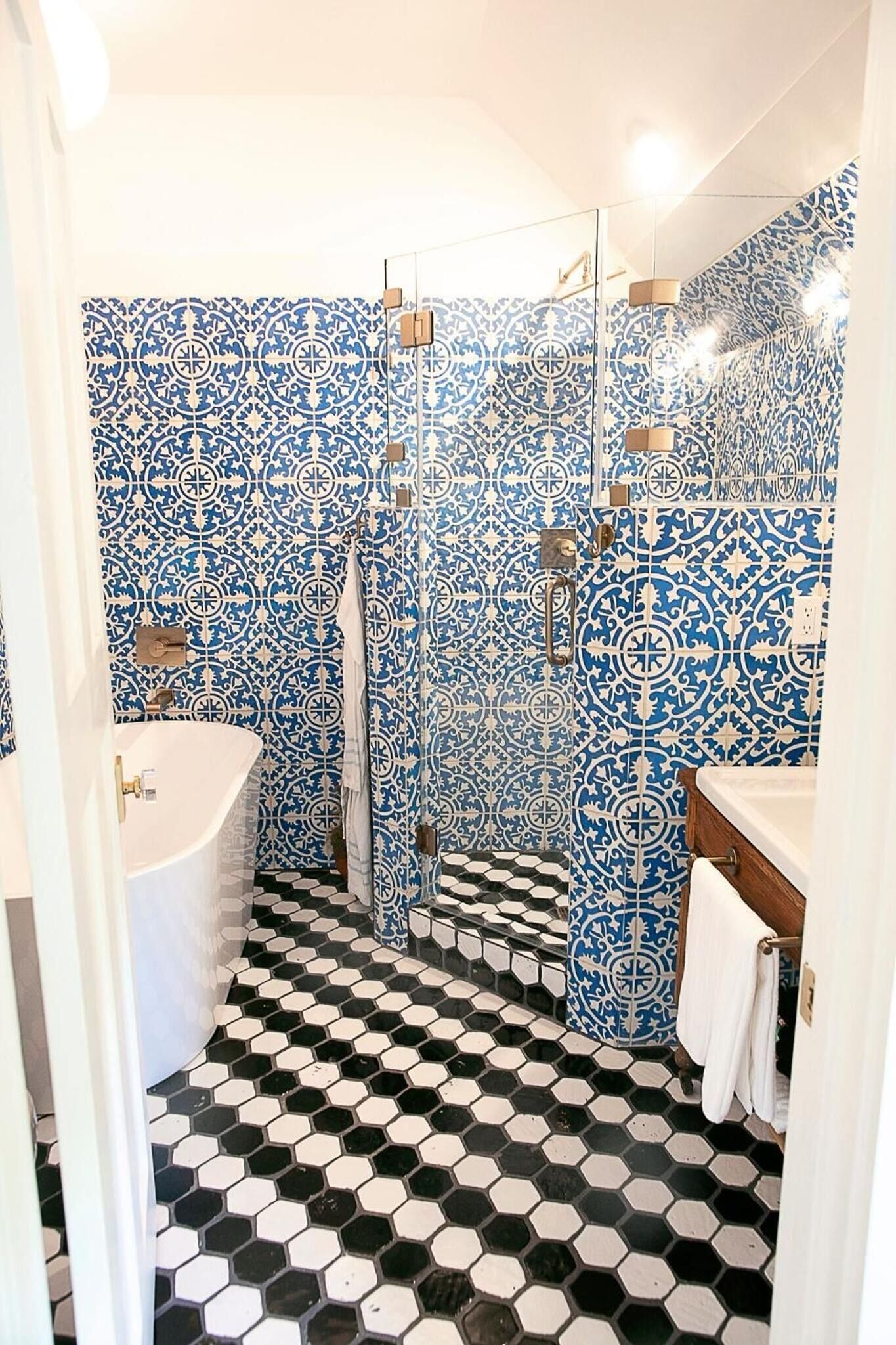 Un baño con baldosas azules y blancas estampadas, piso de baldosas hexagonales en blanco y negro, y una bañera blanca.