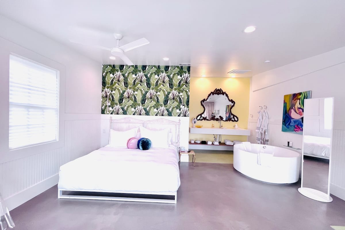 A modern bedroom with a bed, a vanity, a bathtub, and a ceiling fan.