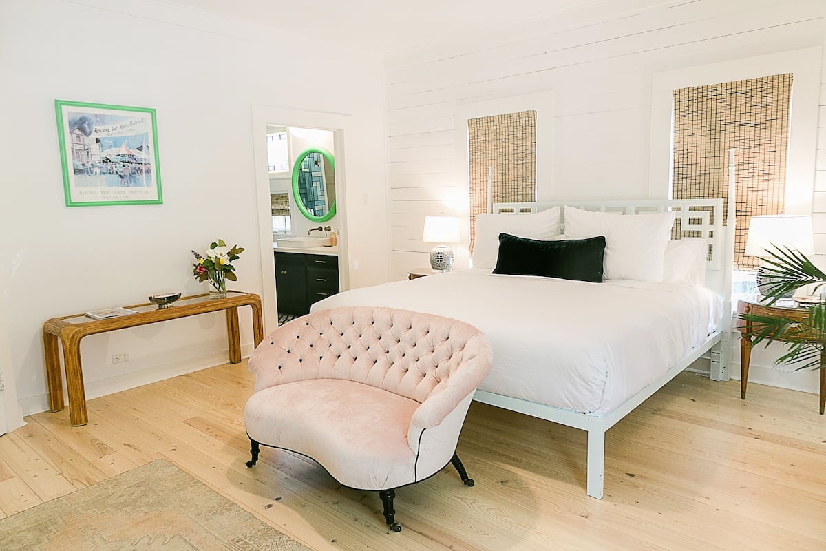 A bedroom with a bed, a chair, a bedside table, and a mirror.