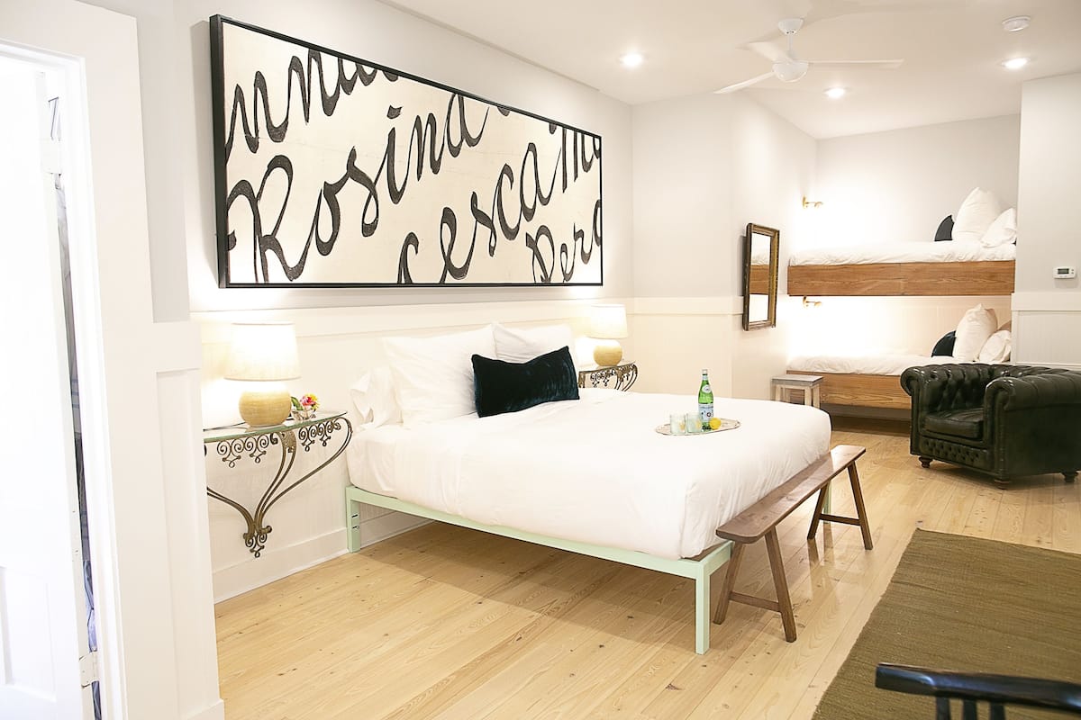 A bedroom with a bed, bedside tables, a bench, a mirror, and a wall art piece.