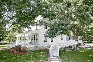 A white two-story house with a covered porch and a small staircase leading to the entrance. - The Frenchie (Round Top)