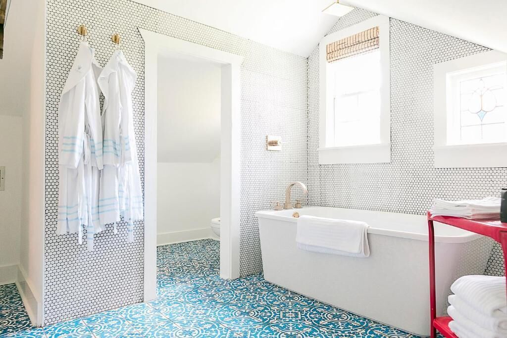 A bathroom with a white bathtub, a red shelf with towels, and a patterned floor.