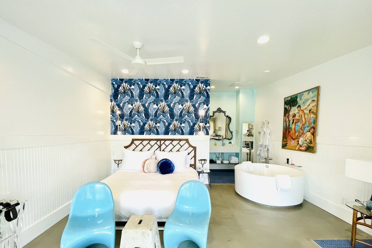 A bedroom with a bed, a vanity, a bathtub, and a painting on the wall.
