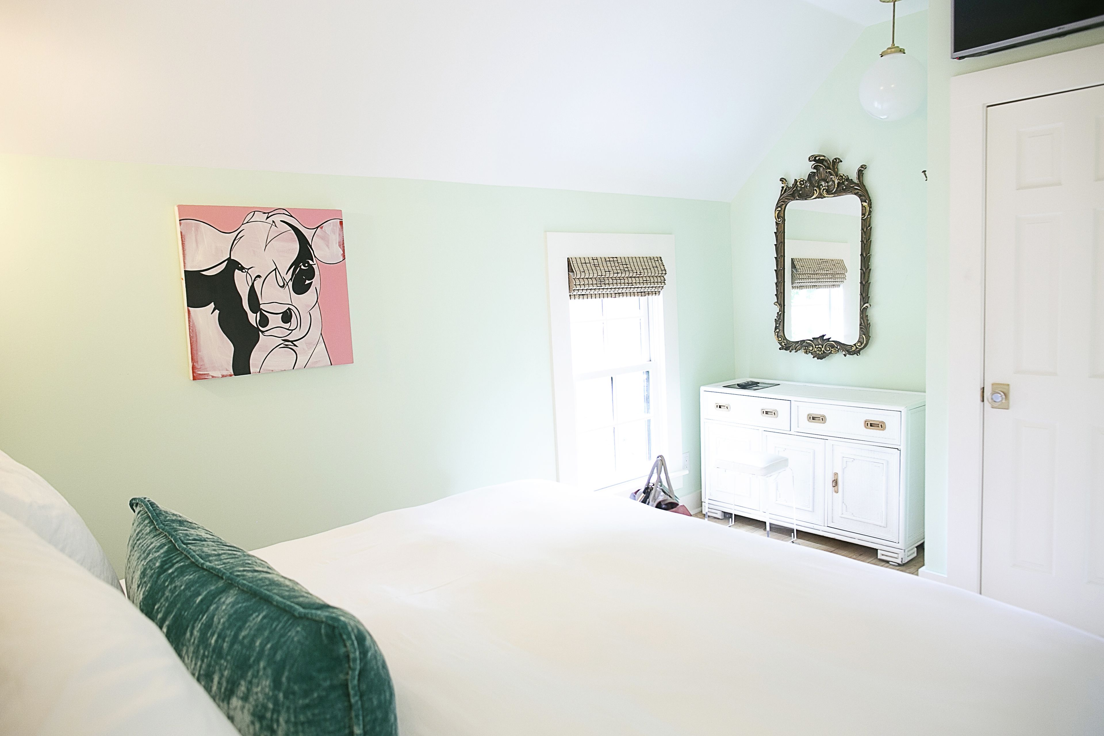 Une chambre à coucher avec un lit, une commode, un miroir et un tableau accroché au mur.