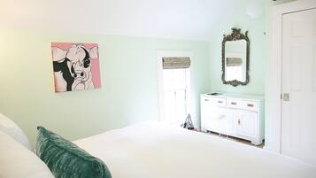 Une chambre à coucher avec un lit, une commode, un miroir et un tableau accroché au mur.