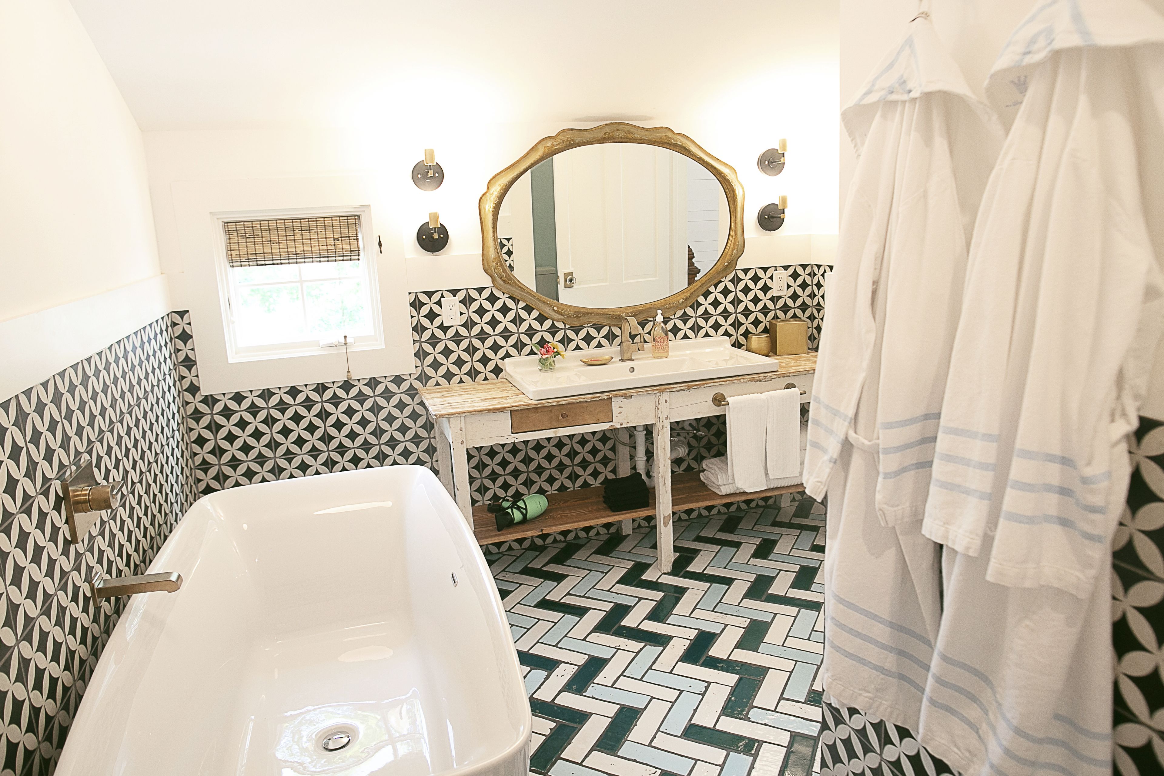 A bathroom with a white sink, a large mirror, and a herringbone-patterned floor.