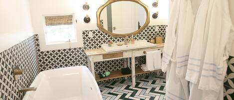 A bathroom with a white sink, a large mirror, and a herringbone-patterned floor.