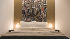 A hotel room with a large bed, two bedside lamps, and a colorful abstract painting on the wall. - Suite Sant 'Agostino behind the cathedral (Palermo)