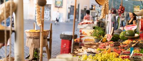 Un puesto de mercado con diversas frutas y verduras, entre ellas uvas, sandía y plátanos.