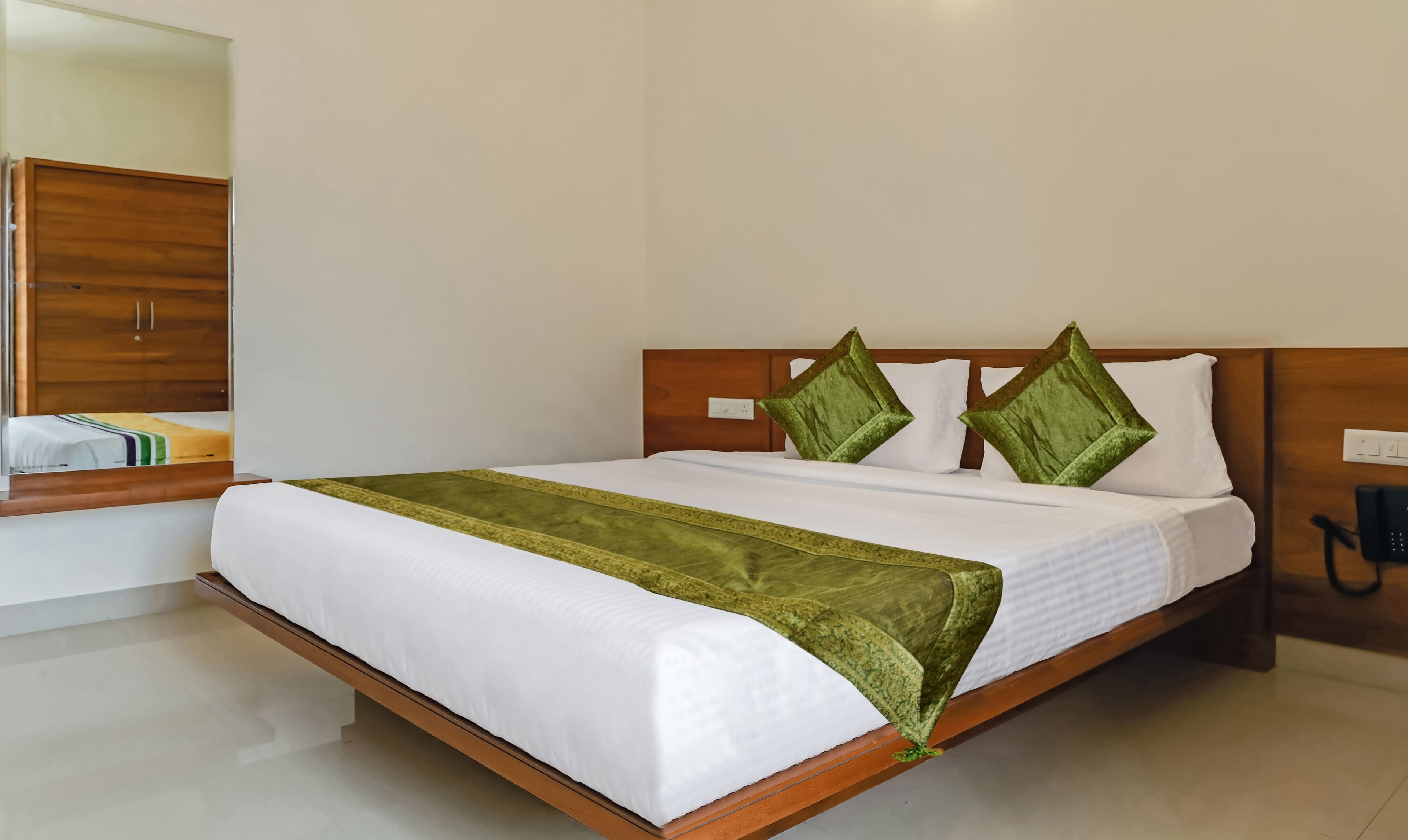 A neatly made bed with white linens and a green throw blanket, a wooden headboard, and two green pillows.