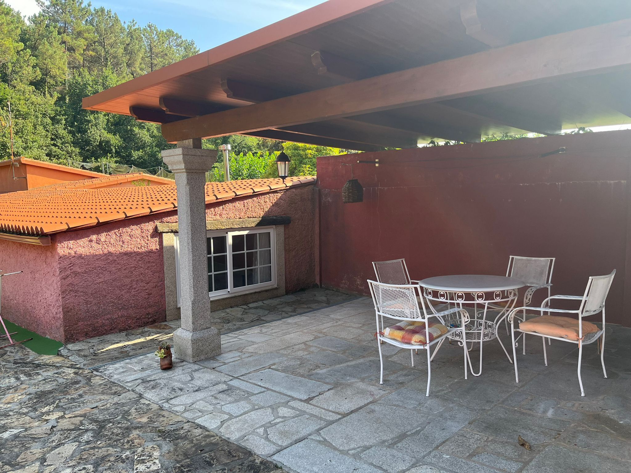 Un patio con mesa y sillas, suelo de piedra y un edificio rojo al fondo.