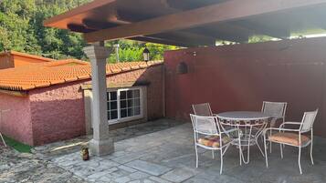 Un patio con mesa y sillas, suelo de piedra y un edificio rojo al fondo.